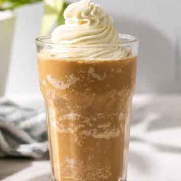 a tall glass filled with frappuccino and topped with whipped cream.